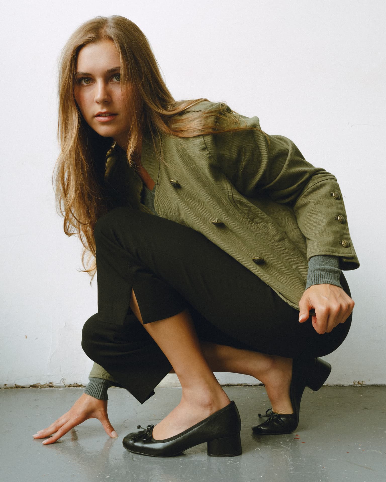 Crouching studio pose in an olive jacket and black trousers