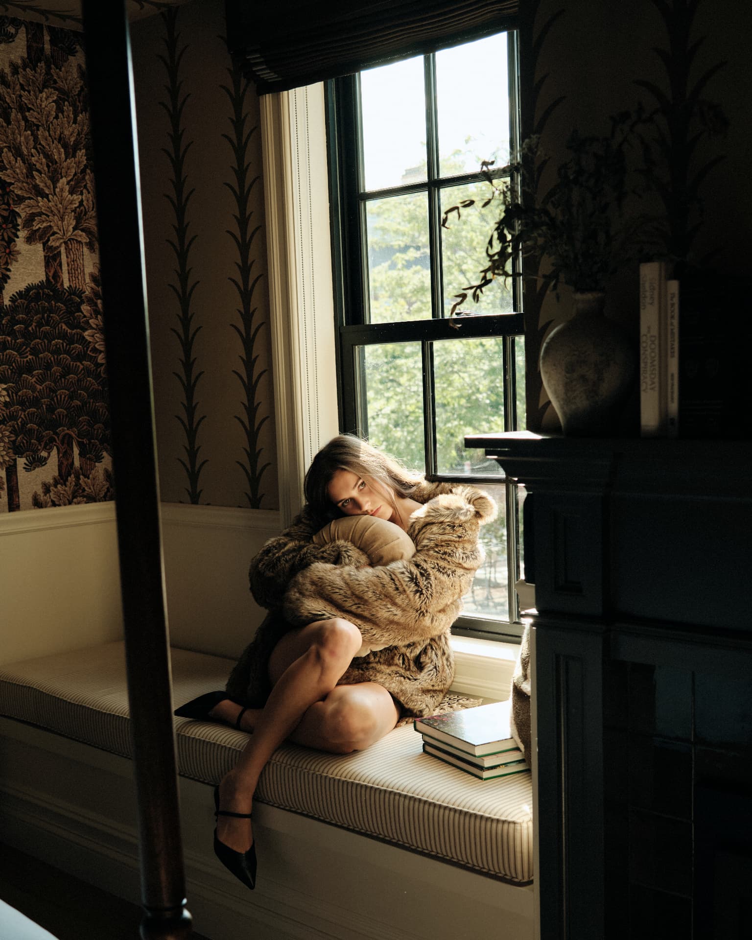 Curled on the window seat hugging a pillow in soft light