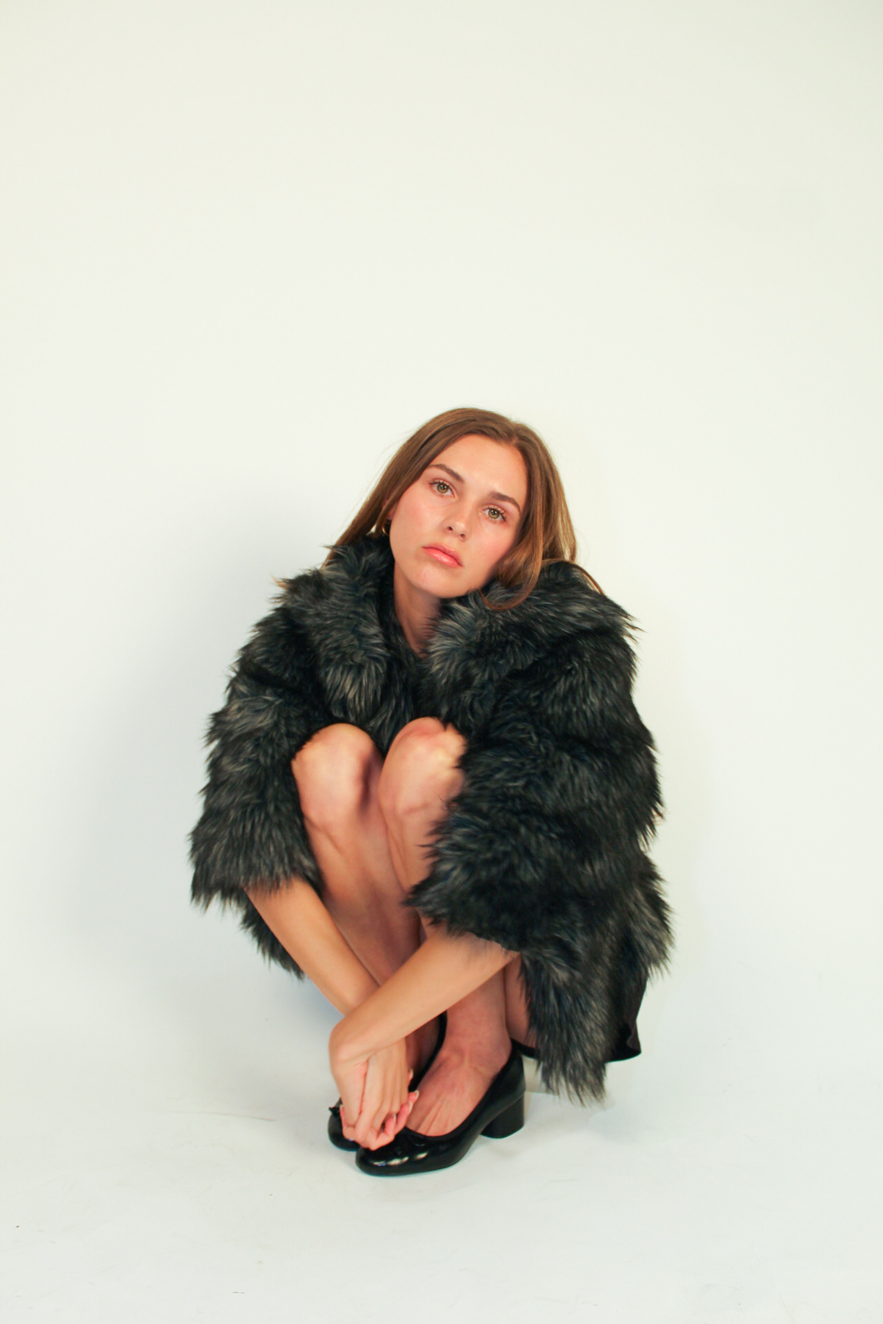 Crouched studio portrait in a black faux fur coat