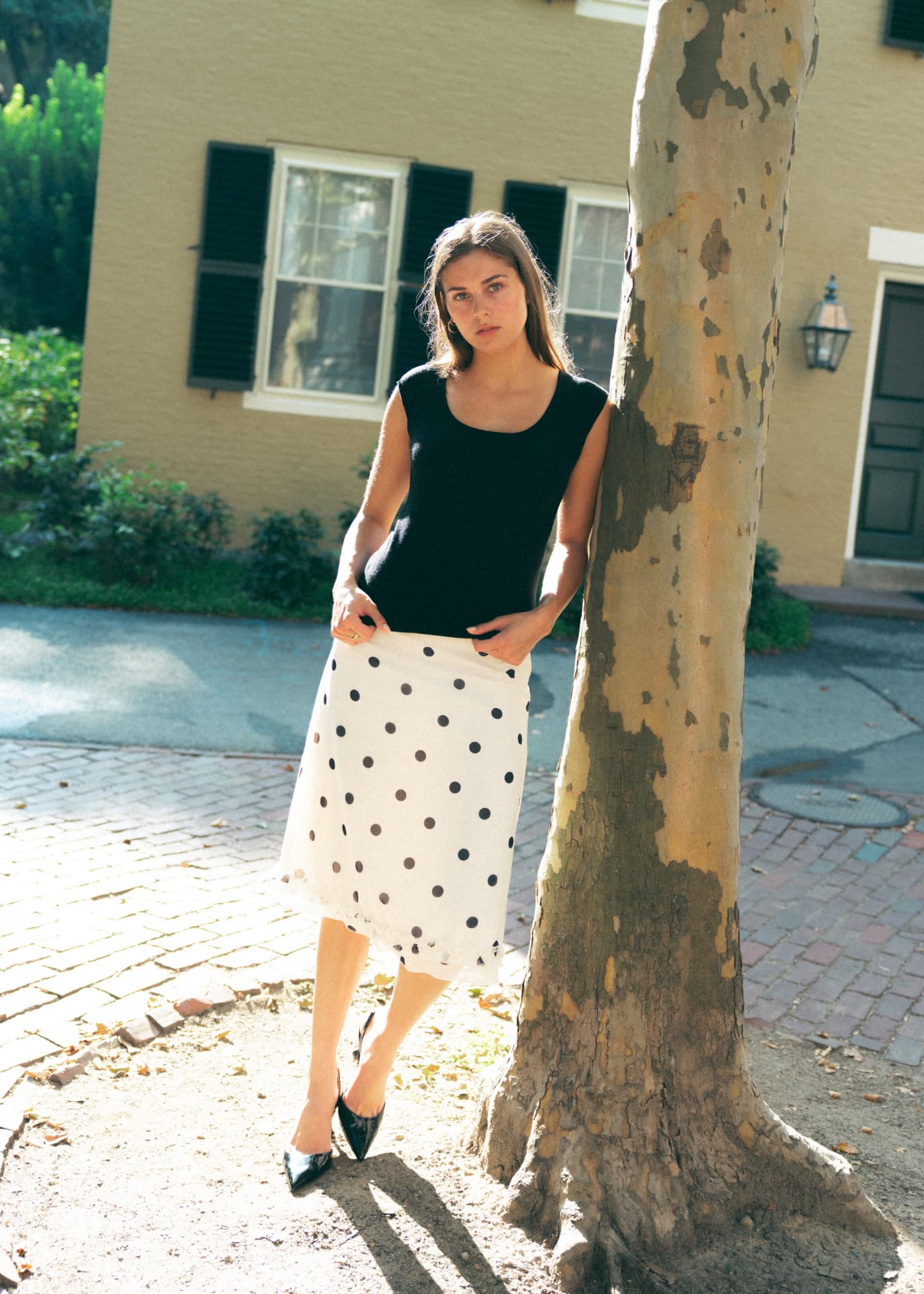 Standing by a sycamore tree in a black knit and polka dot skirt